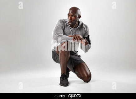 Porträt von hübschen jungen afrikanischen Männermodel kniend auf grauem Hintergrund und wegsehen. Stockfoto