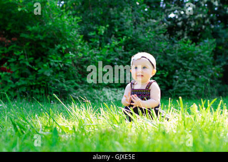 Babymädchen an etwa 6 Monate alt im Freien in einer natürlichen Umgebung mit vorhandenem Licht für ein Lifestyle-Porträt. Stockfoto