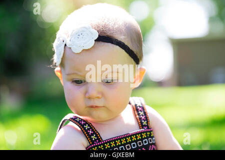 Babymädchen an etwa 6 Monate alt im Freien in einer natürlichen Umgebung mit vorhandenem Licht für ein Lifestyle-Porträt. Stockfoto