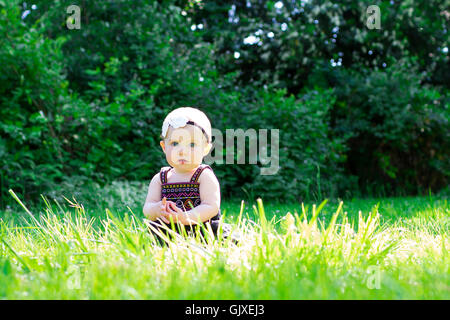 Babymädchen an etwa 6 Monate alt im Freien in einer natürlichen Umgebung mit vorhandenem Licht für ein Lifestyle-Porträt. Stockfoto