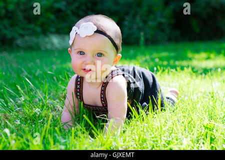 Babymädchen an etwa 6 Monate alt im Freien in einer natürlichen Umgebung mit vorhandenem Licht für ein Lifestyle-Porträt. Stockfoto