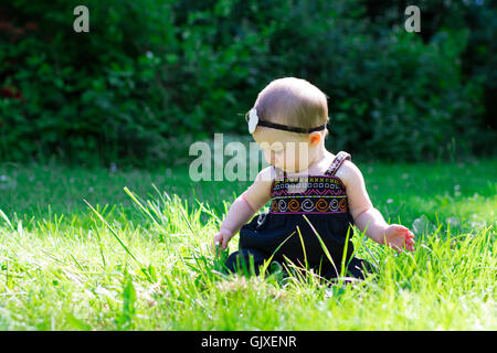 Babymädchen an etwa 6 Monate alt im Freien in einer natürlichen Umgebung mit vorhandenem Licht für ein Lifestyle-Porträt. Stockfoto