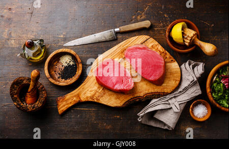 Rohen Thunfisch Steaks Filet mit Zitrone und Sesam auf Olivenholz Schneidebrett auf dunklem Holz Stockfoto