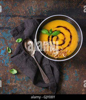 Schwarze Keramik Schüssel mit Kürbis und Süßkartoffeln Creme Suppe mit frischem Basilikum, gebratenen Zwiebeln und Balsamico-Sauce serviert mit Löffel auf Stockfoto