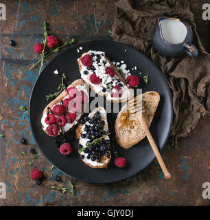 Eingestellt von Dessert-Sandwiches mit frischen Beeren Heidelbeeren und Himbeeren, Frischkäse, Thymian und Honig, serviert mit Krug Milch auf Stockfoto