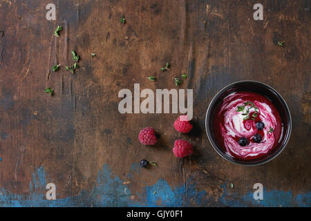 Schwarzen Keramikschale Himbeer Dessert Suppe mit Sahne, serviert mit frischen Beeren und Thymian über alte Holz strukturierten Hintergrund. Stockfoto