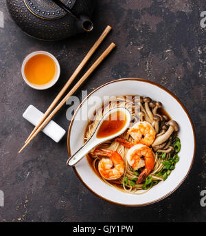 Asiatische Ramen-Nudeln mit Garnelen, Shimidzhi Pilzen und Frühlingszwiebeln in Brühe und Tee auf dunklem Hintergrund Stockfoto