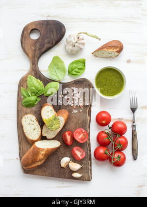 Hausgemachte Pesto-Sauce, frisches Brot, Cherry-Tomaten auf dunkel rustikalen Holzbrett über weiß lackierten hölzernen Hintergrund, top Stockfoto