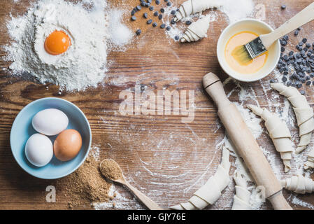 Backzutaten für das Kochen von Croissants. Eiern, brauner Zucker, geschmolzene Butter, Mehl, Schokolade-Chips über rustikale Holz Zeitmessung Stockfoto