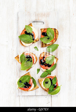 Caprese-Sandwiches mit Tomaten, Mozzarella, Basilikum und Balsamico-Glasur auf weißen gemalten hölzernen Hintergrund, Draufsicht, vertic Stockfoto