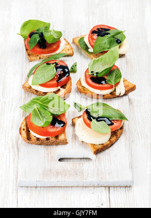 Caprese-Sandwiches mit Tomaten, Mozzarella, Basilikum und Balsamico-Glasur auf gemalte Tafel über leichten hölzernen Hintergrund, Stockfoto