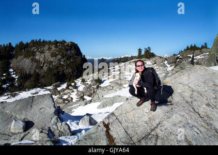 Chinesischen kanadischen Mann, Wandern mit Hund Jack Russell auf British Columbias Mount Seymour mit schneebedeckten Berge und blauer Himmel Stockfoto