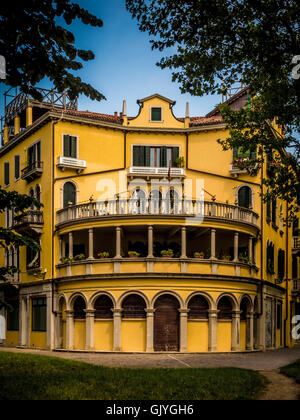 Geschwungene Außenwand eines traditionellen, gelb gerafften Gebäudes mit Bogentür und Fenstern. Venedig, Italien. Stockfoto