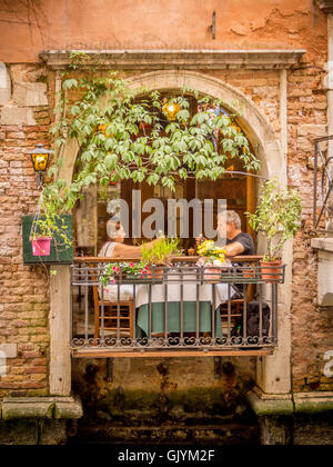 Älteres paar Essen auf einen Balkon mit Blick auf einen Kanal in Venedig, Italien. Stockfoto