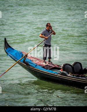 Gondoliere tragen traditionelle gestreiftes Top Lenkung seine Gondel, während auf seinem Handy zu sprechen. Venedig, Italien. Stockfoto