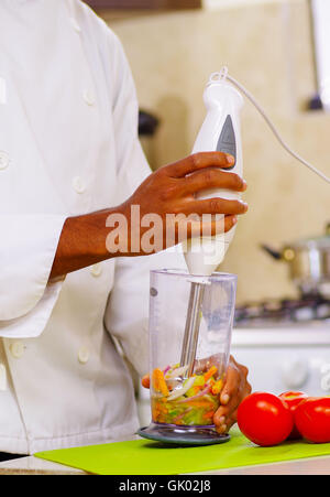 Closeup Händen der Chef vermischen buntem Gemüse aus transparentem Glas mit Handheld-Mixer, Profi-Küche, weißer Hintergrund Stockfoto
