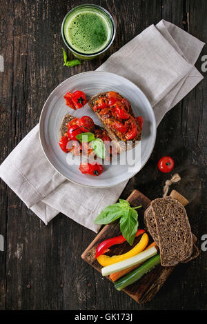 Italienische Tomaten-Bruschetta mit gebackenen Kirschtomaten und geschnittenem Gemüse, serviert auf graue Keramik-Platte mit textilen Serviette und Stockfoto