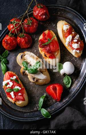 Diverse Mini-Bruschetta mit Tomaten, Feta-Käse, Huhn, Pilze, Erdbeeren und Basilikum auf geröstetem Baguette serviert auf Stockfoto