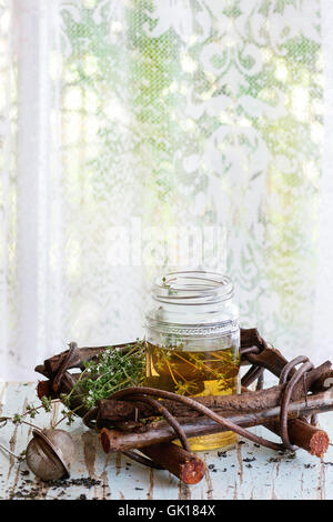 Glas heißer Kräutertee mit Bund frischer Thymian, serviert mit Vintage Teesieb auf alten Holzstuhl mit Fenster im backg Stockfoto