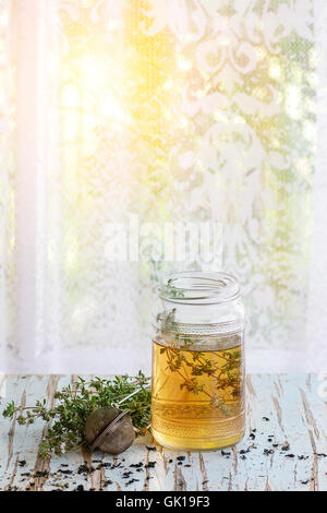 Glas heißer Kräutertee mit Bund frischer Thymian, serviert mit Vintage Teesieb auf alten Holzstuhl mit Fenster im backg Stockfoto