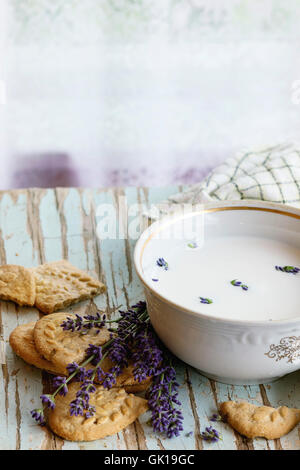 Lavendel Cookies und Schüssel aromatischen Milch serviert mit Küchentuch auf alten Holztisch mit Fenster im Hintergrund. Frühstück i Stockfoto