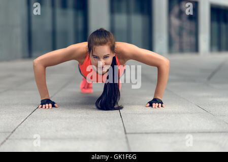 Fit junge Frau dabei drücken-uns in der Stadt in ihre Sportbekleidung, blickte in die Kamera lächelnd, frontal niedrigen Winkel Ansicht Stockfoto