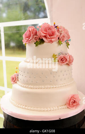 Weiße Hochzeitstorte mit rosa Blumen auf einem Tisch in einem Zelt. Stockfoto