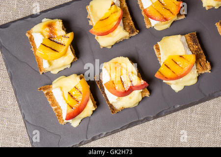 Kanapees, Vorspeise mit gegrilltem Brie und Nektarine auf einer Schiefertafel Schale vergoldet Stockfoto