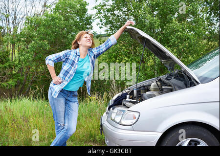 Frau mit Schraubenschlüssel in der Nähe von ihr kaputtes Auto Stockfoto