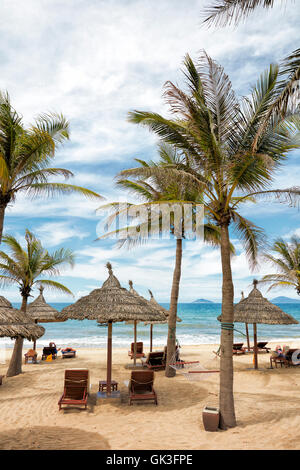 Liegestühle und Strohschirme unter Palmen am Cua Dai Beach. Hoi An, Provinz Quang Nam, Vietnam. Stockfoto