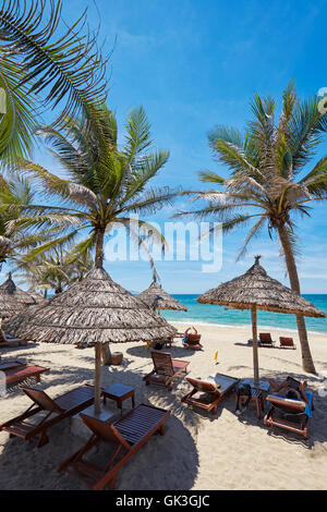 Liegestühle unter strohgedeckten Sonnenschirmen auf Cua Dai Beach. Hoi An, Provinz Quang Nam, Vietnam. Stockfoto