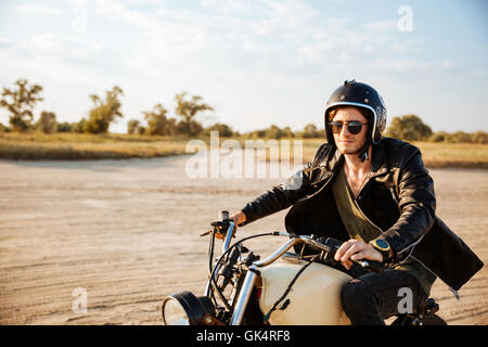 Brutale Jüngling in einer schwarzen Jacke und Brille Retro-Motorrad fahren Stockfoto