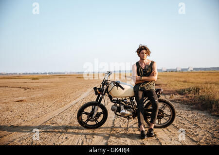 Brutale Jüngling in schwarz stützte sich auf ein Motorrad Stockfoto