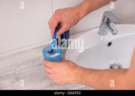 Mannes Hände waschen ein Rasiermesser in der Tasse mit Wasser in der Nähe von Waschbecken in das modern geflieste Bad zu Hause Stockfoto