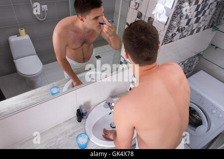 Blick von oben auf einen jungen Mann, die Rasur mit einer Razer stand vor Spiegel mit Waschbecken in das modern geflieste Bad an Stockfoto