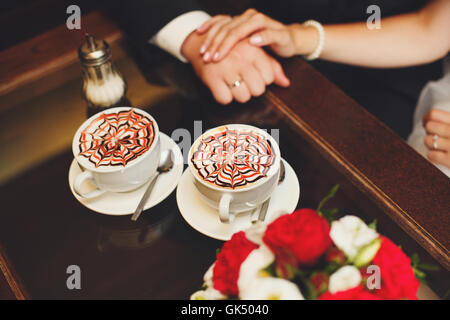 Hände der Braut und des Bräutigams auf Tisch, Latte Kaffee Tassen Stockfoto