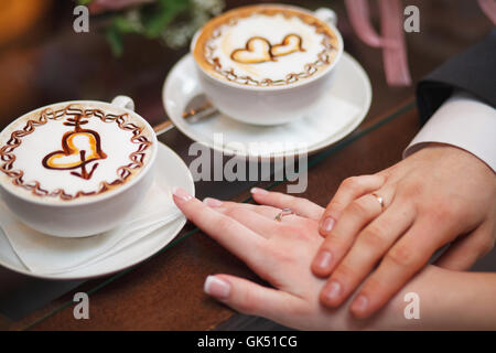 Hände der Braut und des Bräutigams auf Tisch, Latte Kaffee Tassen Stockfoto