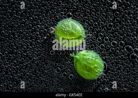 Stachelbeeren Früchte in Mineralwasser, eine Reihe von Fotos. Close-up kohlensäurehaltiges Wasser vor schwarzem Hintergrund Stockfoto