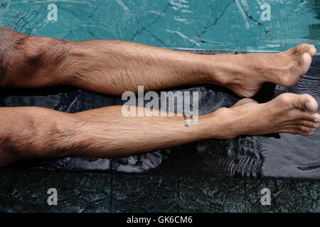 Mans Beine an der Seite eines Schwimmbades in Bali Stockfoto