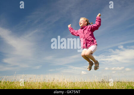 junges Mädchen springen auf einer grünen Wiese vor blauem Himmel Stockfoto