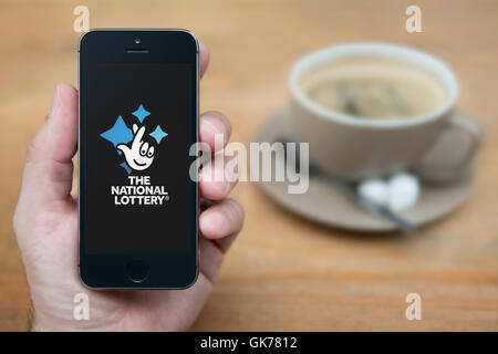 Ein Mann schaut auf seinem iPhone die National Lottery-Logo anzeigt, während bei einer Tasse Kaffee (nur zur redaktionellen Verwendung) saß. Stockfoto