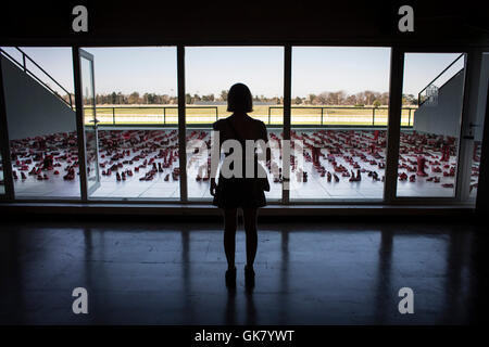 San Isidro, Argentinien. 18. August 2016. Eine Frau wacht die Installation Kunstschau "Rote Schuhe" auf der Art Space Fair, in der Stadt San Isidro, 30 km von Buenos Aires, der Hauptstadt von Argentinien, am 18. August 2016. Die mexikanische Künstlerin Elina Chauvet konzipiert die Arbeit als eine kollektive Reflexion über Gewalt gegen Frauen, da sie ihre Schwester, weil es verloren. Chauvet Werk wurde ursprünglich vorgestellt, in Ciudad Juarez, Mexiko, und später in mehreren anderen mexikanischen und ausländischen Städten, wo Menschen Hunderte von roten Schuhen auf der Messe gespendet. Bildnachweis: Martin Zabala/Xinhua/Alamy Live-Nachrichten Stockfoto