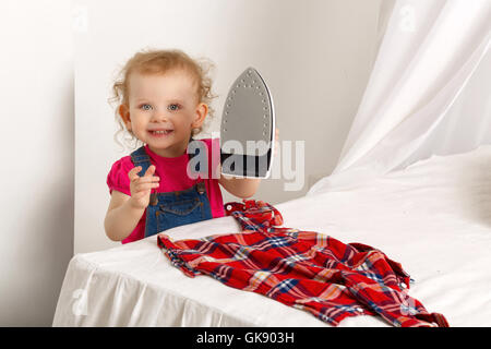 Ein kleines Mädchen mit Eisen auf Eisen kariertes Hemd. Mamas Helfer. Hausarbeit. Stockfoto