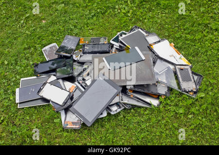 Grosser Haufen die gebrochenen und gerissenen zellulären Telephons und Tabletten liegen auf dem grünen Rasen Rasen. Moderne Technologien verschmutzen enviro Stockfoto