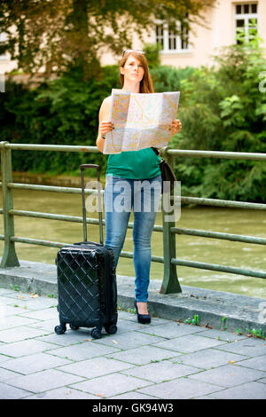 junge Brünette Frau stehend mit ihren Koffer und mit Blick auf einen Stadtplan Stockfoto