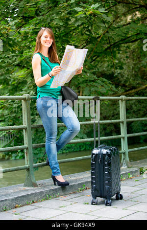 junge Brünette Frau stehend mit Koffer und ein Blick auf Karte Stockfoto