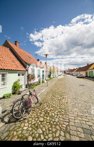Zwei Fahrräder abgestellt auf einer gepflasterten Straße mit kleinen hübschen Hütten. Stora Norregatan, Simrishamn, Skane / Scania, Schweden. Stockfoto