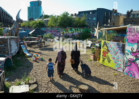 Lokalen muslimischen Familie gehen vorbei an Graffiti und Installationskunst im nomadischen Gemeinschaftsgärten Space in Shoreditch, Brick Lane. London.UK Stockfoto