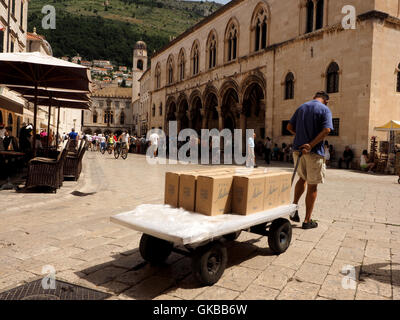 Mann in kurzen Hosen ziehen einen Wagen beladen mit Karton Kartons in Pred Dvorom in der ummauerten Altstadt von Dubrovnik-Kroatien Stockfoto