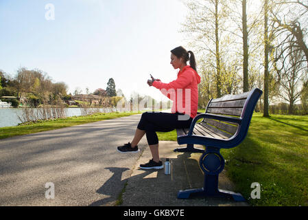 Junge Frau sitzt auf Parkbank Activity Tracker überprüfen Stockfoto